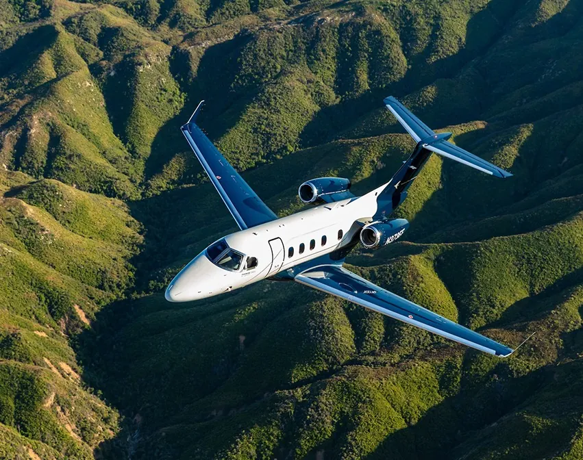 Embraer Phenom 300EV business jet in flight over green hills, equipped with Garmin Autoland